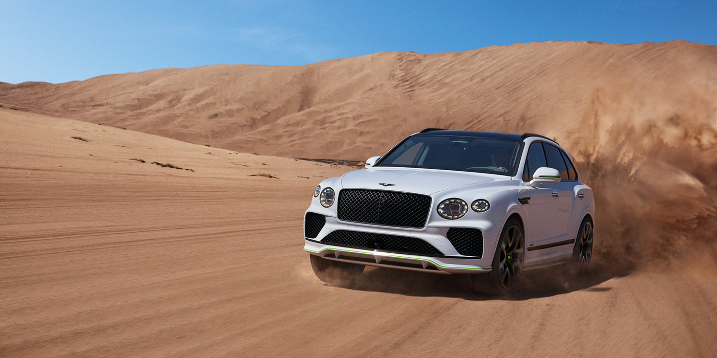 Bentley Istanbul Bentley Bentayga Speed SUV front three quarter in Snow Quarts Pearlescent by Mulliner white paint driving dynamically through the desert
