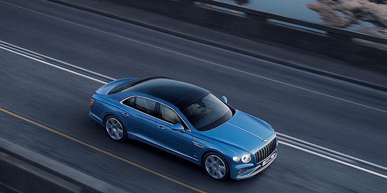 Bentley Istanbul New Bentley Flying Spur Azure sedan in Light windsor blue paint by Mulliner, with 22 inch Azure wheels seen from overhead driving dynamically on a country road