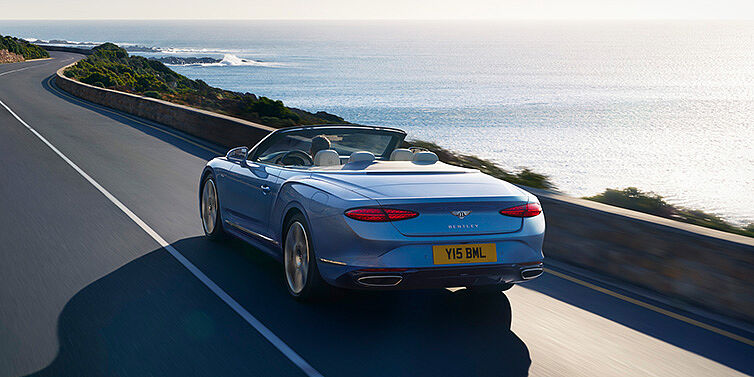 Bentley Istanbul New Bentley Continental GTC Azure convertible rear view in Light Windsor blue paint with 22 inch ten spoke wheels driving dynamically on an ocean road in the sunshine